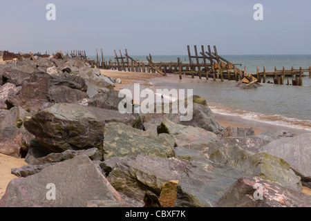 Happisburgh Beach, North Norfolk. Rotto brakewaters legname importato e rocce di granito posizionati riducono la forza delle maree in entrata Foto Stock