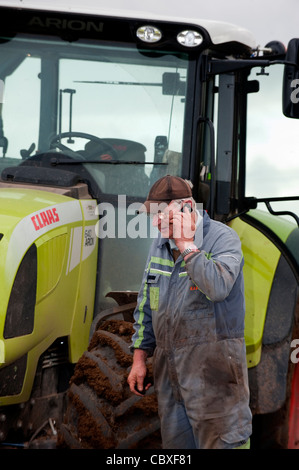 Agricoltore parlando al telefono cellulare mentre in piedi di fronte a trattore fermo. Foto Stock