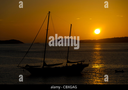 GALLOWS POINT, St. John, Isole Vergini americane: Una barca a vela a due alberi si staglia contro il sole al tramonto mentre è ormeggiata nelle acque calme al largo di Gallows Point a St. John, Isole Vergini americane. Questa pittoresca scena cattura la miscela di tradizione nautica e bellezza naturale che caratterizza l'isola caraibica. Foto Stock