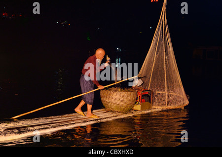 Notte cinese pescatore cormorano di sollevamento con il pesce in un cestello sul fiume Li in Yangshuo Repubblica Popolare Cinese Foto Stock