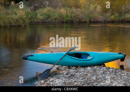 Blue whitewater kayak su una spiaggia rocciosa contro il fiume con il colore oro riflessione Foto Stock