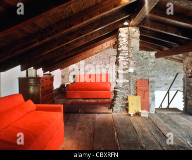 Soppalco con divano letto rosso e le pareti sono di pietra e il pavimento è di legno in una vecchia casa per le vacanze Foto Stock