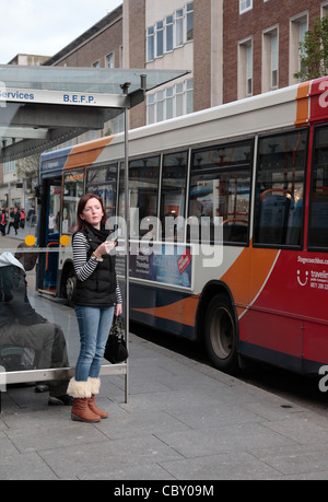 Ragazza con smart phone presso la fermata degli autobus con Stagecoach single decker bus Foto Stock