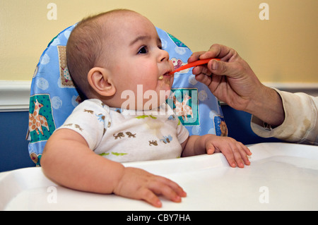 Otto mesi di età bambino essendo alimentato ananas organico dal Padre che è appena tornato a casa dal lavoro Foto Stock