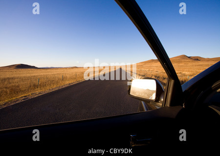 Veduta laterale auto specchio con road passando attraverso il campo in background Foto Stock