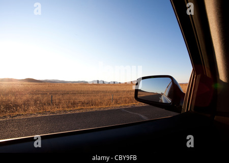 Veduta laterale auto specchio con road passando attraverso il campo in background Foto Stock