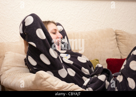 Giovane donna vestito nella sua Vestaglia recante su un divano sbadigli Foto Stock