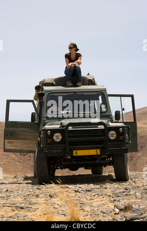 Giovane donna seduta sulla parte superiore del veicolo safari - Purros Conservancy - Kaokoland, Regione di Kunene, Namibia, Africa Foto Stock