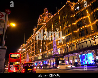I grandi magazzini Harrods al tramonto con le luci di Natale shoppers e passaggio di taxi e autobus rossi Knightsbridge London SW1 Foto Stock
