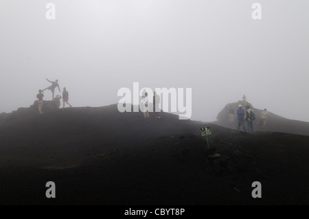 VULCANO PACAYA, Guatemala: Un gruppo di turisti posa per delle foto su una cima nuvolosa e nebbiosa del vulcano Pacaya. Pacaya è un vulcano attivo che fa parte dell'arco vulcanico dell'America centrale. Costituisce una popolare destinazione turistica facilmente accessibile da Antigua e città del Guatemala. Situato all'interno del Parco Nazionale Pacaya, si erge a 2.552 metri (8.373 piedi). La sua ultima grande eruzione, che causò una notevole damange ai villaggi vicini e rimodellò la cima, fu nel maggio 2010. Quell'eruzione e la cenere vulcanica sparsa su gran parte della zona vicina, provocando la chiusura delle scuole e l'evacuazione di emergenza Foto Stock