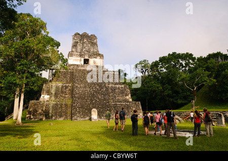 Tempio Tikal II Tempio delle Maschere Guatemala // TIKAL, Guatemala - i turisti si riuniscono nella grande piazza prima del Tempio II, noto anche come il Tempio delle Maschere, nel Parco Nazionale di Tikal. Le moderne scale in legno installate sul lato sinistro della piramide consentono ai visitatori di salire vicino alla cima della struttura di 125 metri. Il tempio, costruito intorno al 700 d.C., rimane uno dei monumenti più visitati di Tikal. Foto Stock