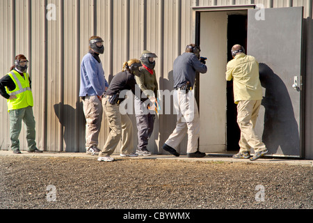 Un lavoro di squadra, maschio e femmina femmina diritto agenti di applicazione pratica di entrare in una stanza con le armi a una CA training facility Foto Stock