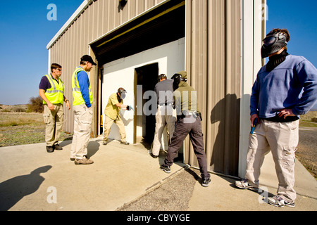 Un lavoro di squadra, maschio e femmina femmina diritto agenti di applicazione pratica di entrare in una stanza con le armi a una CA training facility Foto Stock