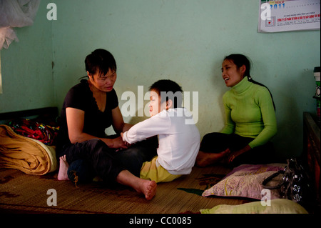 Femmina treni fisioterapista genitore a prendersi cura del bambino con handicap nella comunità basata del programma di risanamento in Vietnam. Foto Stock