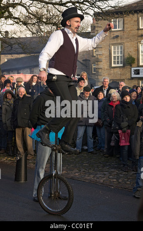 Un animatore di strada su una uni-cycle intrattiene la folla della Grassington Dickensian Festival di Natale, North Yorkshire Foto Stock