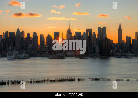 Il sole splende attraverso gli edifici del centro di Manhattan skyline di sunrise come visto nel New Jersey. Foto Stock