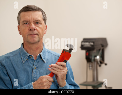 Senior maschile in una officina di casa di fronte alla macchina fotografica e in possesso di una chiave dinamometrica di grandi dimensioni Foto Stock