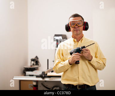 Senior maschile in una officina di casa di fronte alla macchina fotografica e tenendo un trapano elettrico Foto Stock