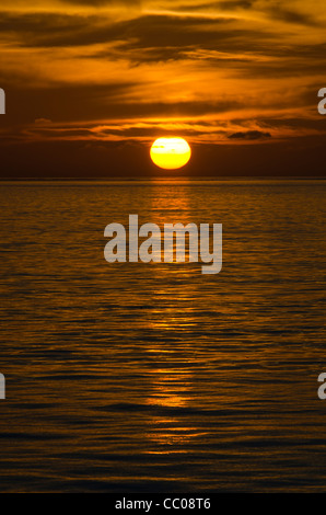 Il Golden Sun scende sotto le nuvole appena prima di colpire l'orizzonte. Il molto calme acque crea una forte riflessione sull'acqua. Prese a Swains Reef sulla estremità meridionale della Grande Barriera Corallina della costa del Queensland, Australia. Foto Stock