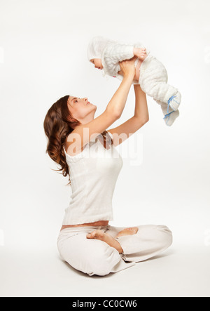Riproduzione di madre con bambino sollevando il suo e seduta in posa di yoga Foto Stock