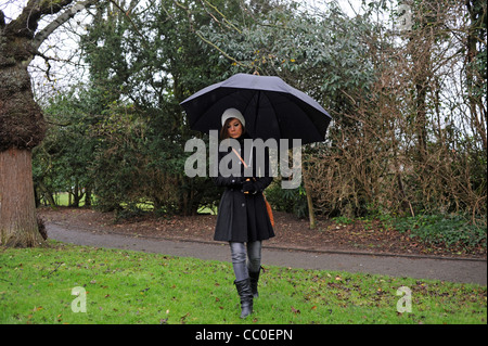 Giovane donna con un grande ombrello nero in un parco di Brighton durante il tempo piovoso Regno Unito (posa da modello) Foto Stock