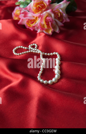 Collana di perle e bouquet di rose su raso rosso fogli Foto Stock