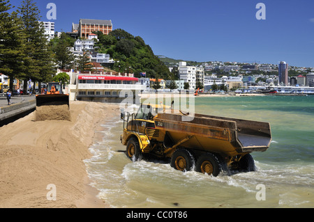 Guida di camion attraverso acqua di mare e le onde al lavoro di rifornimento della spiaggia (la spiaggia riceve una nuova partita di sabbia) a Oriental Bay, Wellington, Nuova Zelanda. Foto Stock