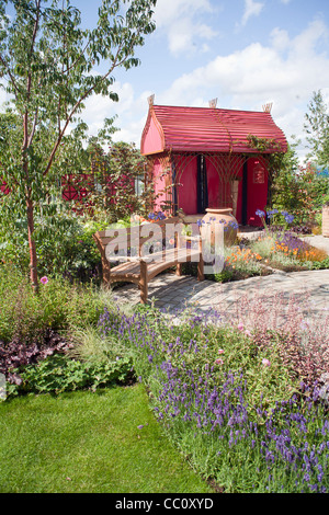 Red pavilion con patio pavimentato, panca in legno, confini e ornamenti. Foto Stock