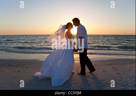 Una coppia sposata, la sposa e lo sposo che si baciano al tramonto su una bella spiaggia tropicale Foto Stock