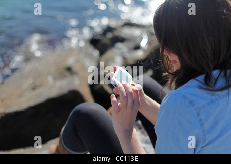 Giovane donna utilizza lo smartphone vicino al mare Foto Stock