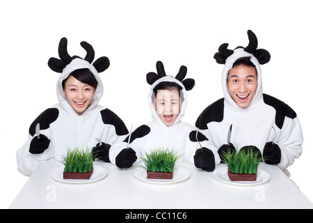 La famiglia in costumi di vacca con porzioni di erba sui loro piastre Foto Stock