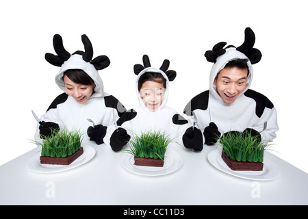 La famiglia in costumi di vacca con porzioni di erba sui loro piastre Foto Stock