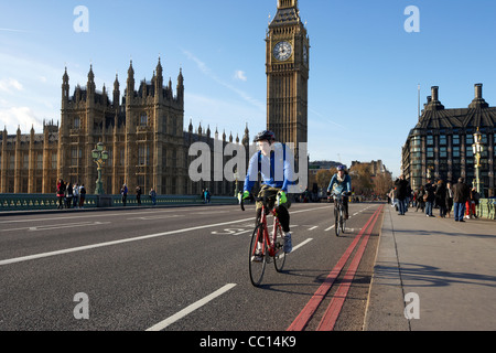 I ciclisti crossing westminster bridge pista ciclabile al di fuori del palazzo di Westminster case di edifici del Parlamento Londra Inghilterra Foto Stock