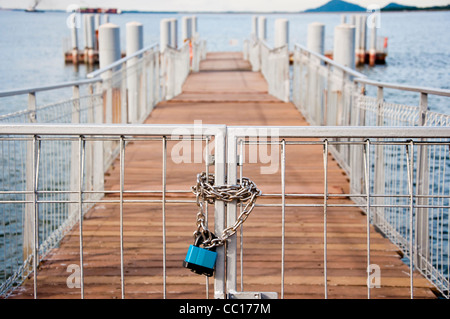Una serratura a catena su di un cancello che conduce al molo a distanza Foto Stock