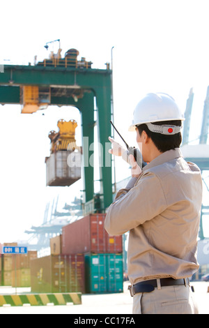 Industria marittima lavoratore dirigere le gru con il suo walkie-talkie Foto Stock