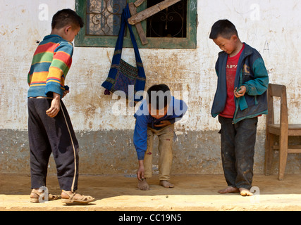 Tre piccoli ragazzi in un villaggio vietnamita giocando a un gioco (marmi) Foto Stock