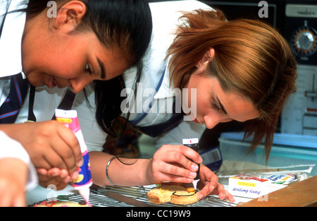 Gli studenti della scuola secondaria torte di glassa nella lezione di cucina di brughiera, scuola, Hounslow, Middlesex, Regno Unito. Foto Stock