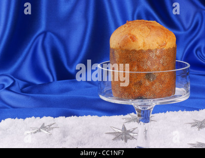 Composizione di natale su un brillante sfondo blu: il panettone, un tipico italiano torta di Natale, servita su una torta di vetro stand Foto Stock