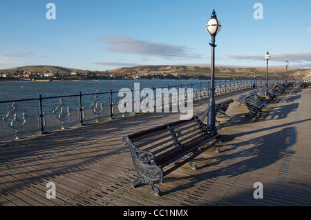 Ghisa panchine, lampioni e ornato di ringhiere, sul lungomare del deserto molo vittoriano a Swanage. Il Dorset, Inghilterra, Regno Unito. Foto Stock