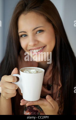 Giovane e bella ragazza con cioccolata calda e sorridente nella parte anteriore della fotocamera Foto Stock