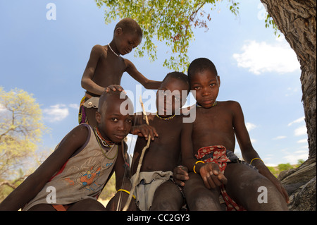 Giovani ragazzi Himba seduti sulle radici di un albero vicino a Ruacana Falls, Kaokoland, Namibia. Foto Stock
