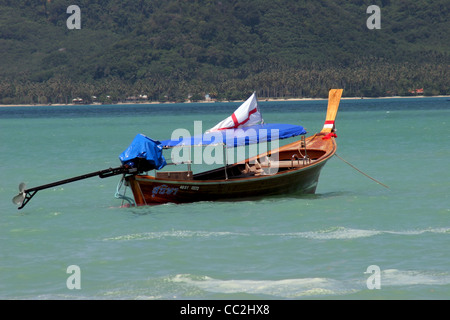 Un longtail barca da pesca è legata al largo di una spiaggia durante la bassa marea in Chalong Bay, Isola di Phuket, Tailandia. Foto Stock