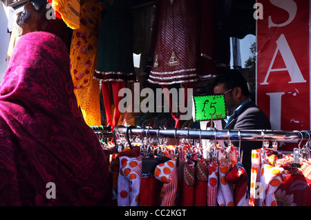 Una donna musulmana guarda attraverso i vestiti in vendita su un mercato in vendita in East End di Londra Foto Stock