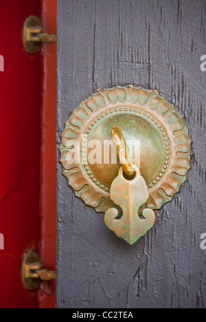 Antica cinese solare manopola di bronzo con una freccia con la maniglia e 2 cerniere su una porta di legno dipinto in grigio e rosso Foto Stock