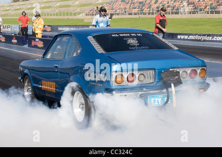 Australian Lee Sanders esegue un pneumatico di fumare la masterizzazione di burnout in gomma nella sua Mazda RX3 propulsori rotante drag racing car. Foto Stock