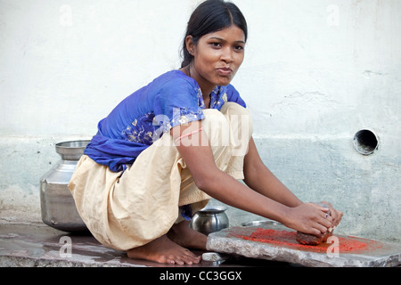 Fare pasta di peperoncino in modo tradizionale con pietra di molatura. vita domestica in India con una bella ragazza indiana in bundi, rajasthan facendo faccende. Foto Stock