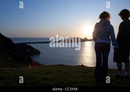 Una giovane coppia Godetevi il tramonto sopra il worm di testa sulla Penisola di Gower, Swansea, Galles del Sud Foto Stock