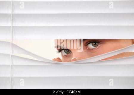 Donna del peering attraverso persiane Foto Stock