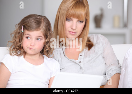 Non impressionati bambina con la madre e un computer portatile Foto Stock