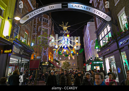 Carnaby Street piena di Natale gli amanti dello shopping a Londra, Inghilterra, Regno Unito, con la festa delle luci decorative di notte Foto Stock